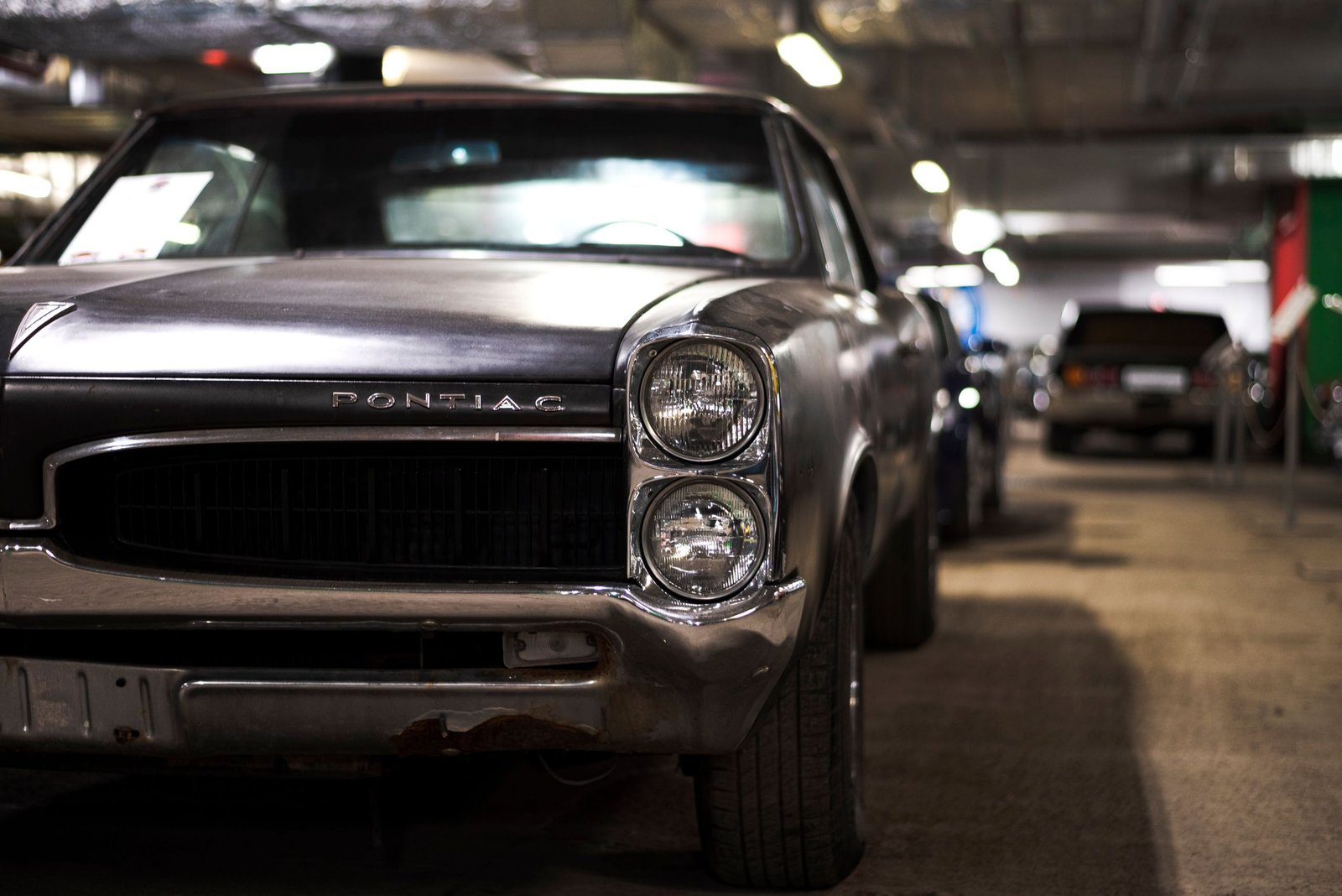 Close-up of vintage Pontiac muscle car parked indoors in an underground garage.